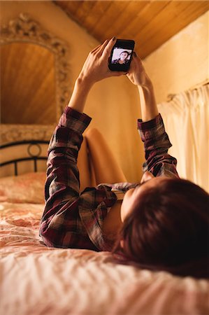 Woman lying on bed and taking a selfie on mobile phone Photographie de stock - Premium Libres de Droits, Code: 6109-08537795