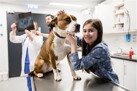 parents consulting doctor - Girl playing with her pet dog while vet discussing x-ray in background Stock Photo - Premium Royalty-Free, Code: 6109-08537862