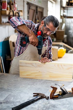 elektrobohrmaschinen - Carpenter drilling a hole in a wooden plank Photographie de stock - Premium Libres de Droits, Code: 6109-08537943