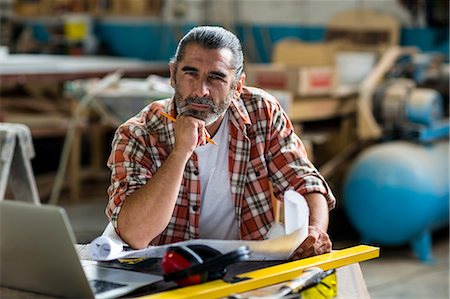 simsearch:6109-08537962,k - Carpenter sitting on workbench with blueprint Stock Photo - Premium Royalty-Free, Code: 6109-08537974