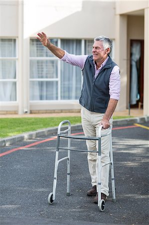 Senior man with walking frame waving his hand outside the hospital Stock Photo - Premium Royalty-Free, Code: 6109-08689530