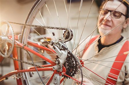 simsearch:614-08873482,k - Portrait of a bike mechanic positioned behind a bike wheel in a workshop Fotografie stock - Premium Royalty-Free, Codice: 6109-08689651
