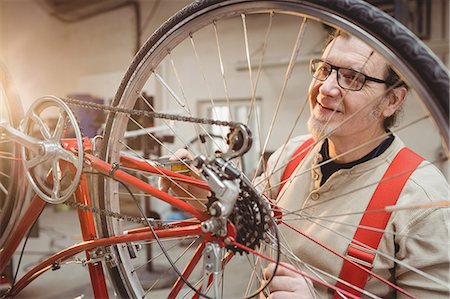 simsearch:614-08873482,k - Portrait of a bike mechanic positioned behind a bike wheel in a workshop Fotografie stock - Premium Royalty-Free, Codice: 6109-08689652