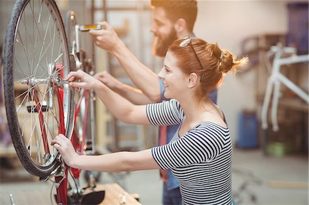 simsearch:6109-08689682,k - Side view of smiling colleague repairing a bicycle in a workshop Stock Photo - Premium Royalty-Free, Code: 6109-08689677
