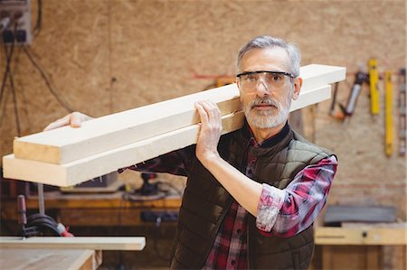 Portrait of a carpenter holding wood plank on his shoulder in a workshop Stock Photo - Premium Royalty-Free, Code: 6109-08689675