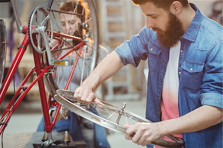simsearch:6109-08689682,k - Side portrait of a hipster repairing a bicycle in a workshop Stock Photo - Premium Royalty-Free, Code: 6109-08689679