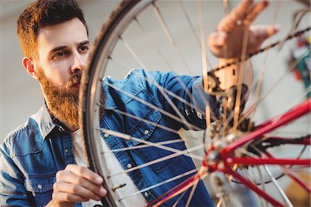 simsearch:6109-08689682,k - Portrait of a hipster repairing a bicycle wheel in a workshop Stock Photo - Premium Royalty-Free, Code: 6109-08689683