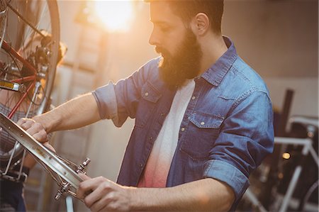 simsearch:6109-08689682,k - Side portrait of a hipster repairing a bicycle in a workshop Stock Photo - Premium Royalty-Free, Code: 6109-08689680