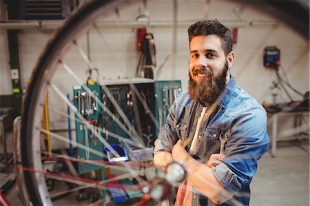 simsearch:6109-08689682,k - Portrait of hipster crossing arms while standing behind a bicycle wheel in a workshop Stock Photo - Premium Royalty-Free, Code: 6109-08689687