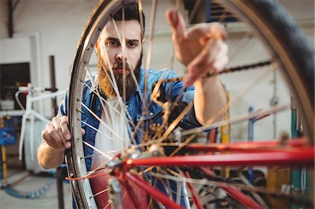 simsearch:6109-08689682,k - Portrait of a hipster repairing a bicycle wheel in a workshop Stock Photo - Premium Royalty-Free, Code: 6109-08689684