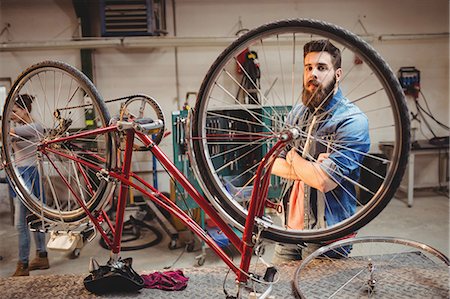 simsearch:6109-08689682,k - Portrait of hipster crossing arms while standing behind a bicycle wheel in a workshop Stock Photo - Premium Royalty-Free, Code: 6109-08689686