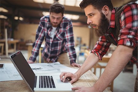 Carpenter using laptop while working on a blueprint in workshop Photographie de stock - Premium Libres de Droits, Code: 6109-08689952