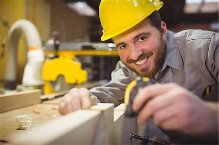 Portrait of carpenter measuring length of wooden plank with measuring tape in workshop Stock Photo - Premium Royalty-Free, Code: 6109-08689923