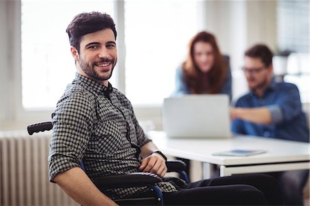 disability - Smiling businessman on wheelchair with coworkers at creative office Foto de stock - Sin royalties Premium, Código: 6109-08690275