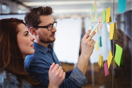 simsearch:6109-08690275,k - Creative business people looking at sticking notes on glass in office Photographie de stock - Premium Libres de Droits, Code: 6109-08690285