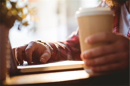 person drink cup of coffee - Cropped image of hipster with laptop and disposable cup at cafeteria Stock Photo - Premium Royalty-Free, Code: 6109-08690361