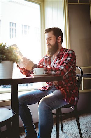 simsearch:6109-08690396,k - Young hipster customer reading from tablet while sitting at cafe Stock Photo - Premium Royalty-Free, Code: 6109-08690364