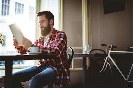 simsearch:6109-08690396,k - Young male customer reading from tablet while sitting at cafeteria Stock Photo - Premium Royalty-Free, Code: 6109-08690365