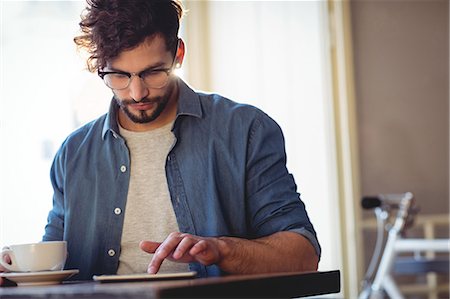 simsearch:6109-08701384,k - Handsome man touching smartphone while sitting with coffee at cafe Foto de stock - Sin royalties Premium, Código: 6109-08690399