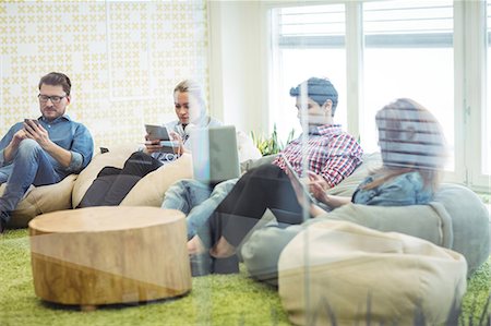 sitting on bean bag - Creative business people using technologies in office seen through glass Stock Photo - Premium Royalty-Free, Code: 6109-08690301