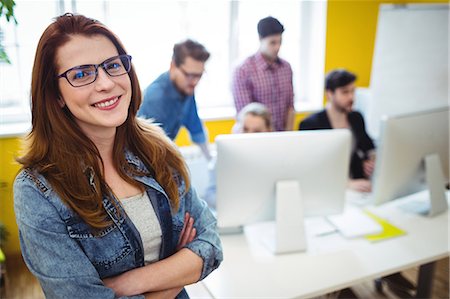 Portrait of happy businesswoman with arms crossed standing against coworkers working in creative ofice Photographie de stock - Premium Libres de Droits, Code: 6109-08690308