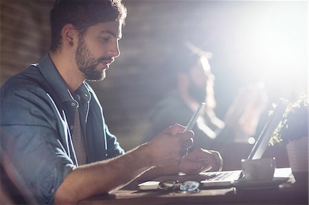 food shop - Side view of handsome young man using cellphone and laptop at cafe Stock Photo - Premium Royalty-Free, Code: 6109-08690411