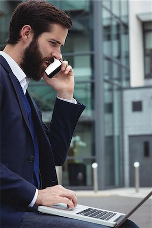 simsearch:6109-08763962,k - Businessman talking on mobile phone while using laptop outside side Stock Photo - Premium Royalty-Free, Code: 6109-08763984