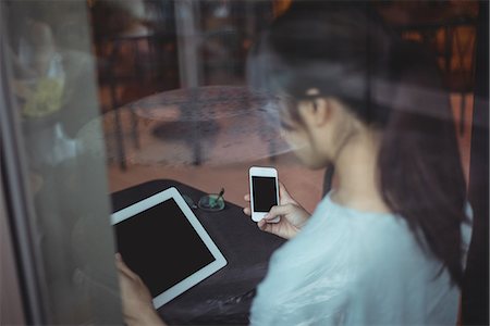 simsearch:6109-08764157,k - Rear view of woman using mobile phone and digital tablet in café Foto de stock - Sin royalties Premium, Código: 6109-08764156