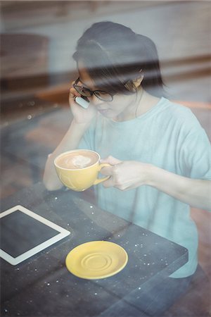 simsearch:6109-07496970,k - Young woman talking on mobile phone while having coffee in café Fotografie stock - Premium Royalty-Free, Codice: 6109-08764163