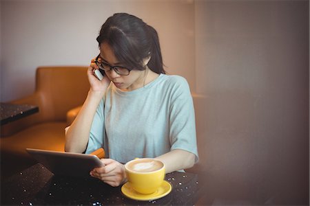 simsearch:6109-08764157,k - Young woman talking on mobile phone while using digital tablet in café Foto de stock - Sin royalties Premium, Código: 6109-08764162