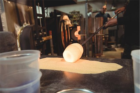 simsearch:693-05794392,k - Glassblower rolling molten glass over frit glass on a marver table at glassblowing factory Stock Photo - Premium Royalty-Free, Code: 6109-08764200
