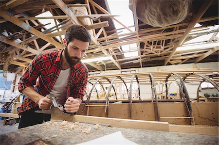 simsearch:6109-08764384,k - Man using hand plane to level the surface of the plank in boatyard Foto de stock - Sin royalties Premium, Código: 6109-08764381