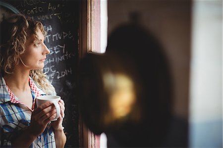 simsearch:6109-08945013,k - Beautiful woman looking through window while having coffee at home Stock Photo - Premium Royalty-Free, Code: 6109-08764423