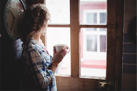 simsearch:6109-08944685,k - Woman looking through window while having coffee at home Stock Photo - Premium Royalty-Free, Code: 6109-08764422