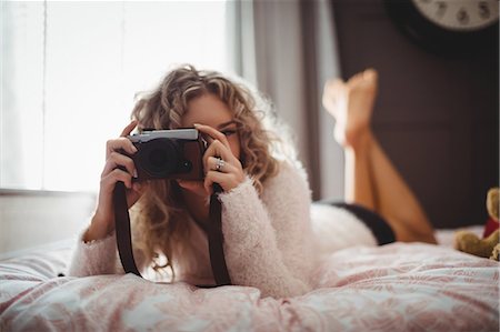 Woman clicking photo from digital camera in bedroom at home Photographie de stock - Premium Libres de Droits, Code: 6109-08764435