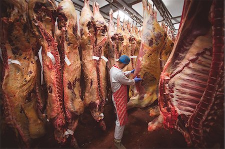 supermarket uniform - Butcher examining the red meat hanging in storage room at butchers shop Stock Photo - Premium Royalty-Free, Code: 6109-08764508