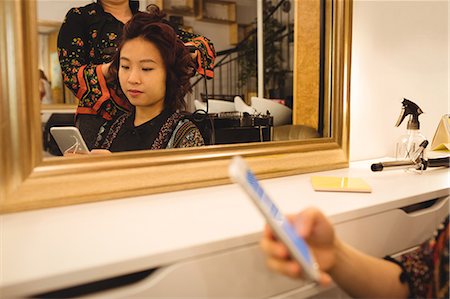 enderezando - Woman using mobile phone while getting her hair straightened at hair saloon Foto de stock - Sin royalties Premium, Código: 6109-08764696