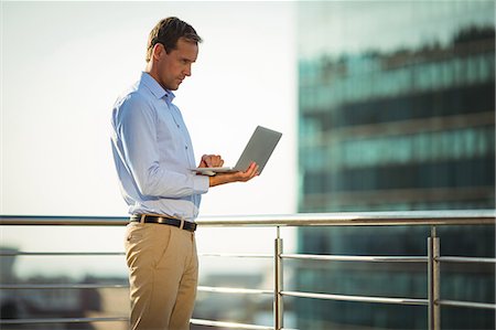 simsearch:6109-08765164,k - Businessman using laptop while standing in balcony at office Fotografie stock - Premium Royalty-Free, Codice: 6109-08765154