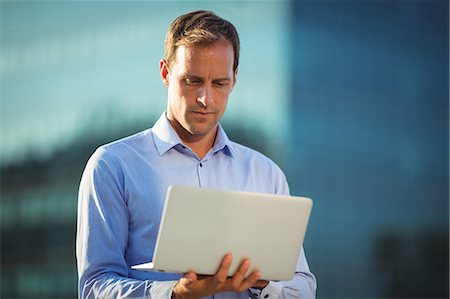 simsearch:6109-08765164,k - Businessman using laptop while standing in balcony at office Fotografie stock - Premium Royalty-Free, Codice: 6109-08765155