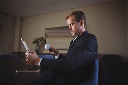 simsearch:6109-08689749,k - Businessman using digital tablet while having coffee in office Photographie de stock - Premium Libres de Droits, Code: 6109-08765187