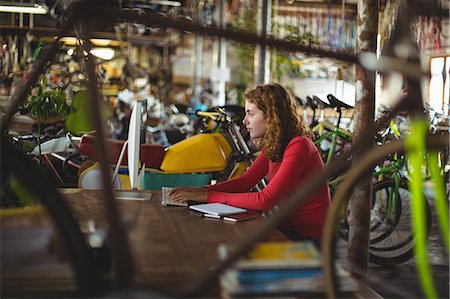 simsearch:6109-08782955,k - Woman sitting at table and using computer in bicycle shop Foto de stock - Sin royalties Premium, Código: 6109-08782864