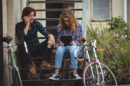 Couple sitting on stairs while talking on mobile phone and using digital tablet Stock Photo - Premium Royalty-Free, Code: 6109-08782930