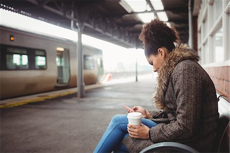 simsearch:6109-08700491,k - Woman using phone while sitting at railway station Foto de stock - Sin royalties Premium, Código: 6109-08700280