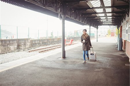 suitcase railway track - Full length of woman carrying baggage while walking at railroad station platform Stock Photo - Premium Royalty-Free, Code: 6109-08700286