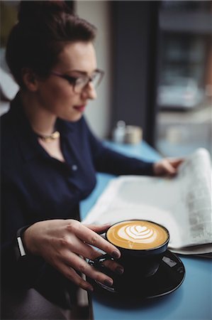 Young businesswoman with coffee cup reading newspaper in cafe Photographie de stock - Premium Libres de Droits, Code: 6109-08700445