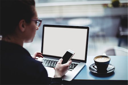 simsearch:6109-08581416,k - Woman with laptop using mobile phone at table in cafe Stock Photo - Premium Royalty-Free, Code: 6109-08700459