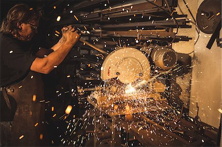 simsearch:6109-08722814,k - Blacksmith using circular saw machine in workshop Foto de stock - Royalty Free Premium, Número: 6109-08700795