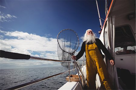 fishing industry - Fisherman holding fishing net and looking at view from boat Stock Photo - Premium Royalty-Free, Code: 6109-08701076