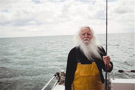 Portrait of fisherman standing on boat holding fishing rod Stock Photo - Premium Royalty-Free, Code: 6109-08701105