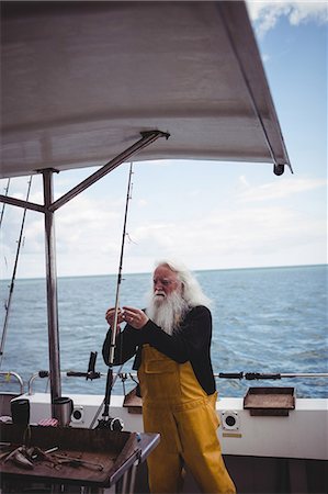 simsearch:6109-08701092,k - Fisherman adjusting fishing hook on fishing boat Photographie de stock - Premium Libres de Droits, Code: 6109-08701121